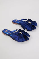 Navy blue flats with large satin bows and pearl embellishments on a neutral background.