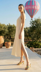 Woman in a white dress standing on a sunlit terrace with a hot air balloon in the background.