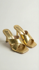 Gold high-heeled sandals on a light gray background