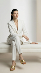 Woman in a white suit sitting on a white bench against a plain background