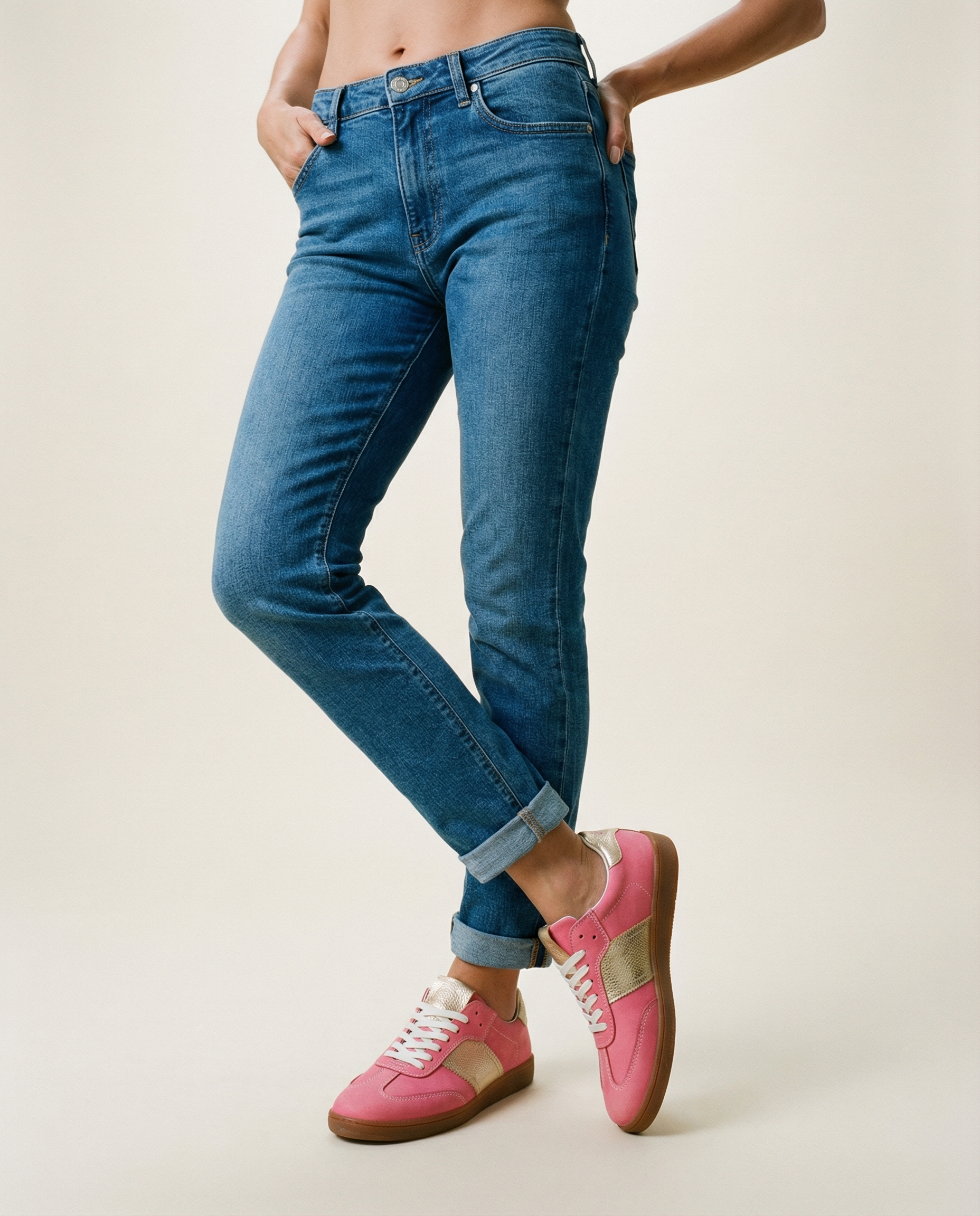 Person wearing blue jeans and pink sneakers on a plain background