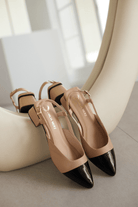 Pair of beige shoes with black pointed toes on a white surface.