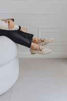 Person wearing beige loafers sitting on a white chair with a neutral background