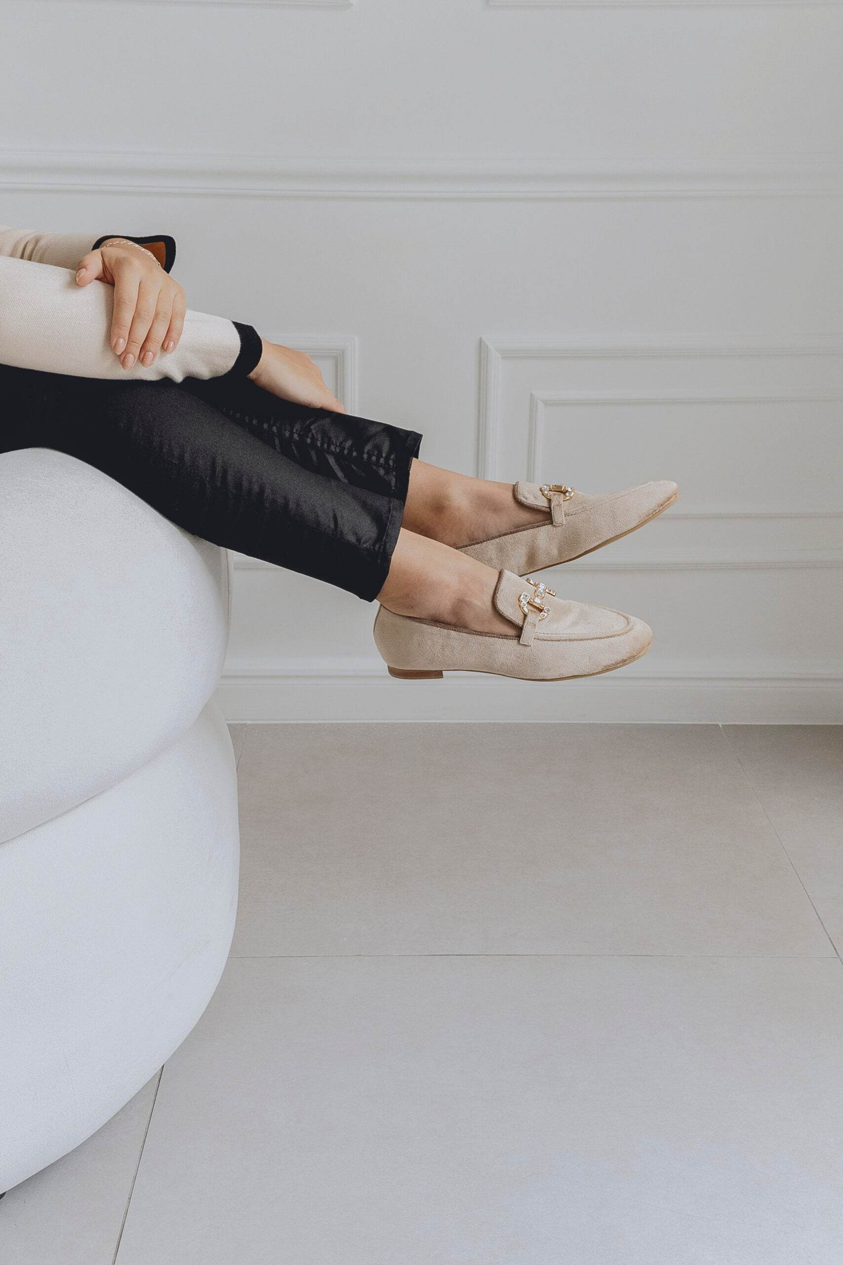 Person wearing beige loafers sitting on a white chair with a neutral background