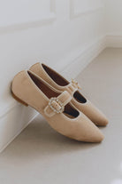 Pair of beige ballet flats with a decorative buckle on a light background