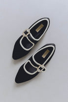 Black pointed-toe shoes with white trim and decorative buckles on a light gray background