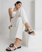 Woman wearing a white outfit with black and white sandals on a white background