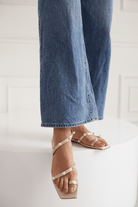 Close-up of legs wearing blue jeans and golden pearl sandals on a white background