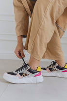 Person wearing beige pants and multi patterned sneakers on a light background