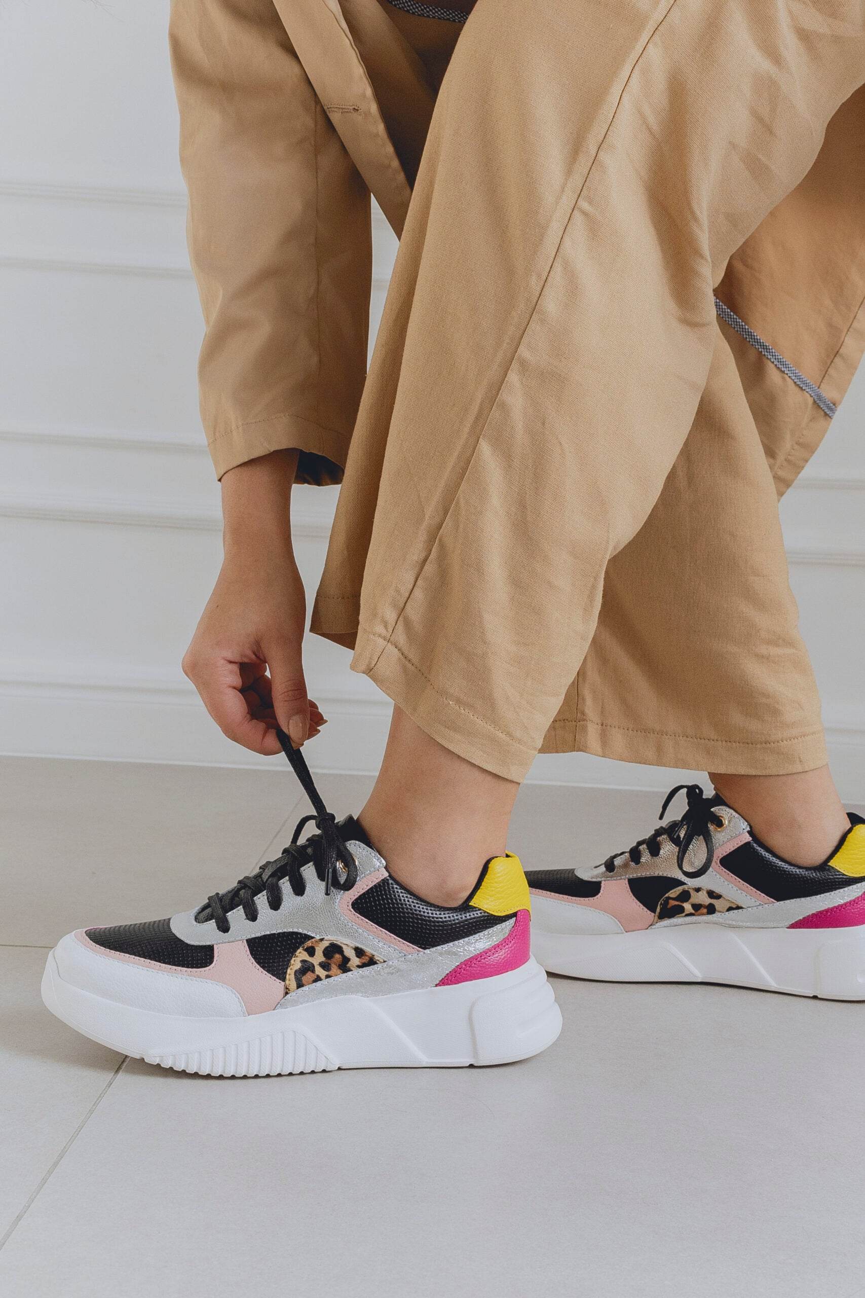 Person wearing beige pants and multi patterned sneakers on a light background