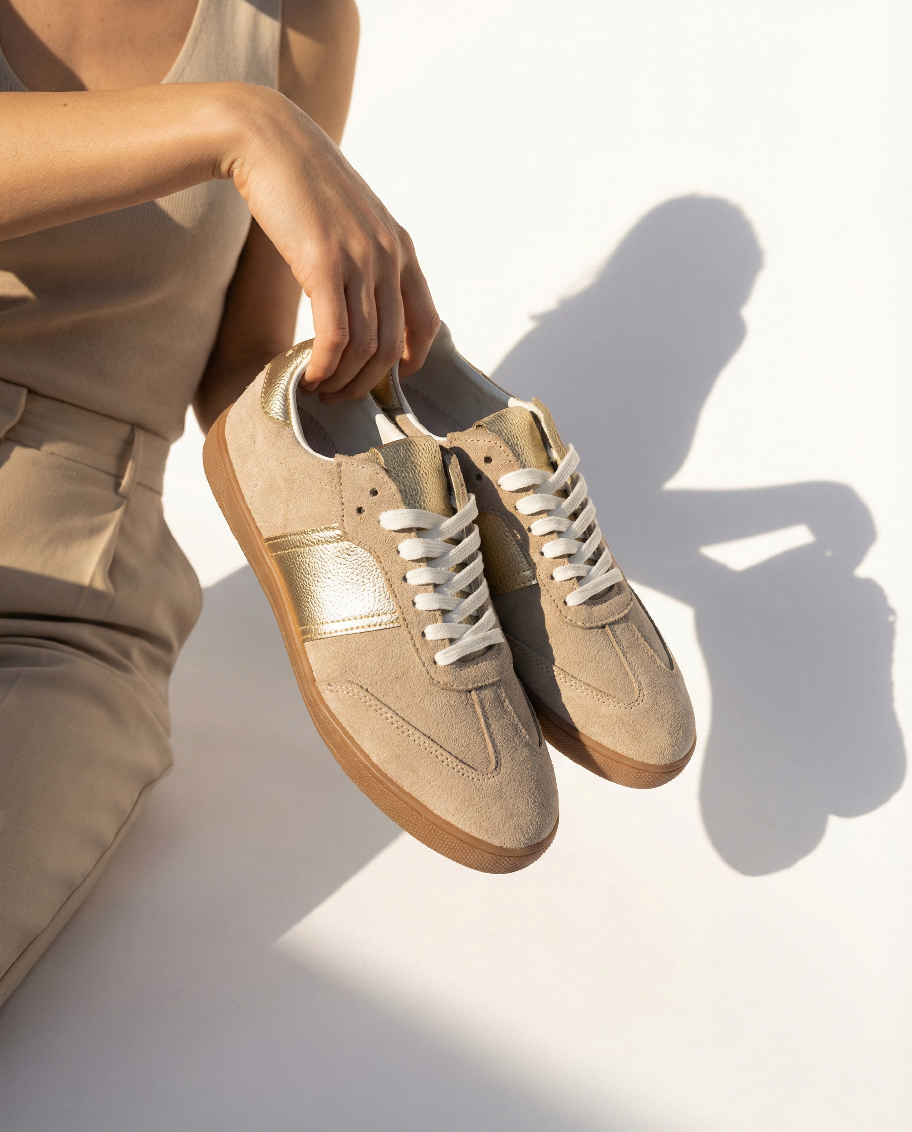 Beige sneakers being held by a person on a light background