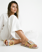 Woman wearing gold and silver sandals with a white outfit on a light background
