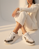 Person wearing white sneakers with leopard print details in a minimalistic setting