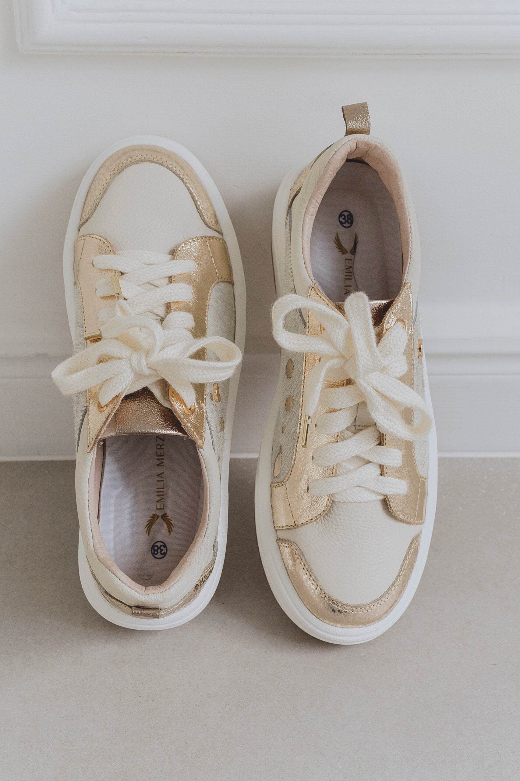 Pair of white sneakers with gold accents on a light background