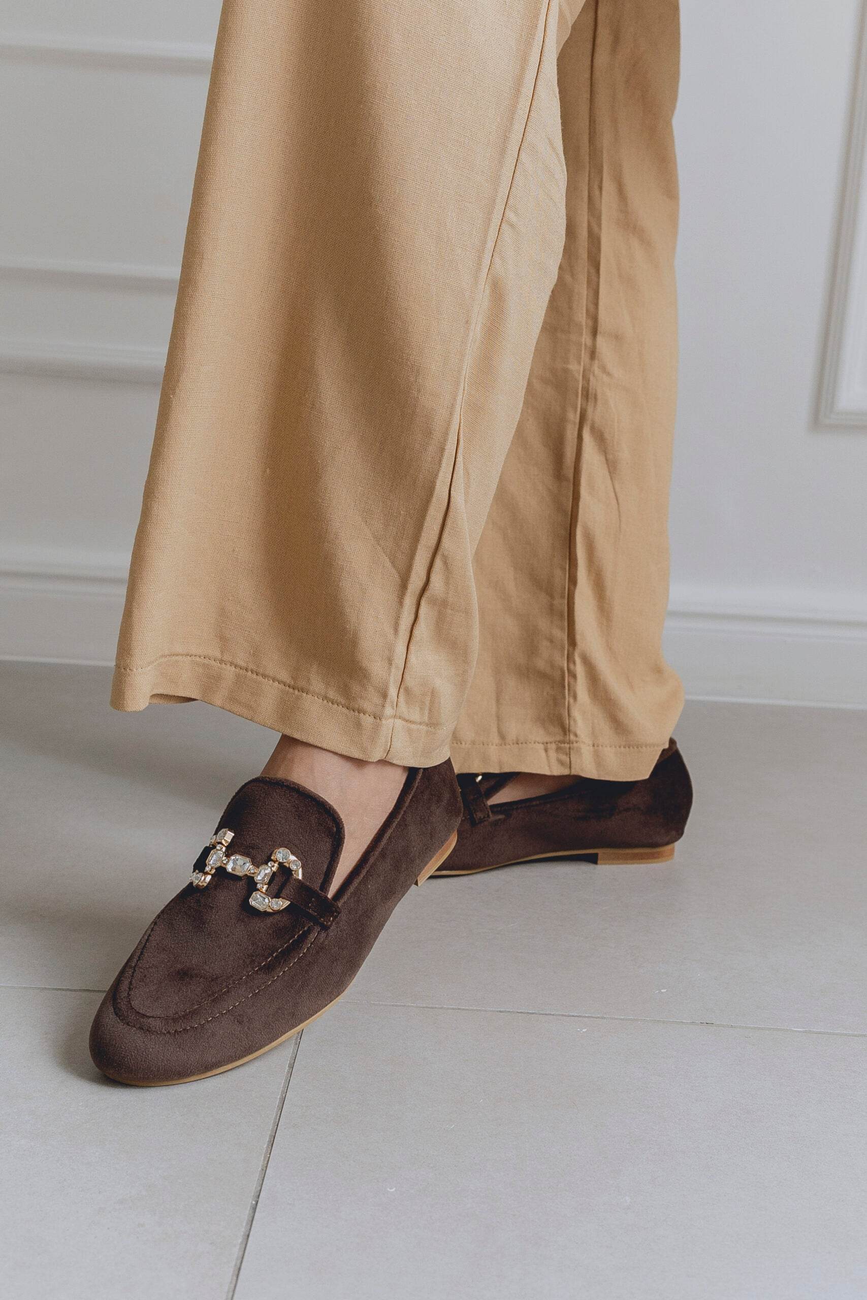 Brown loafers worn with beige pants on a light wooden floor.