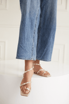 Close-up of blue jeans and gold sandals with pearls on a white background