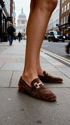 Brown loafers with gold accents worn on a city street.