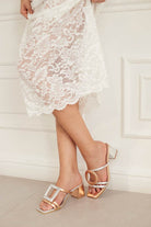 Person wearing a white lace dress and rosegold high-heeled sandals on a light background