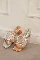Pair of rosegold and silver high-heeled sandals on a neutral background