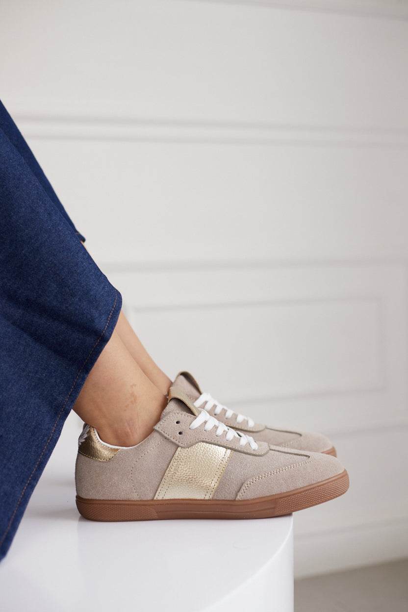 Beige sneakers with brown soles worn by a person in a blue outfit on a white background