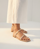 Gold sandals with pearls worn with a white dress on a light gray background