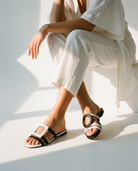 Person wearing black and white sandals with a white outfit on a light background