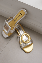 Asymmetrical gold and silver sandal on a light wooden floor