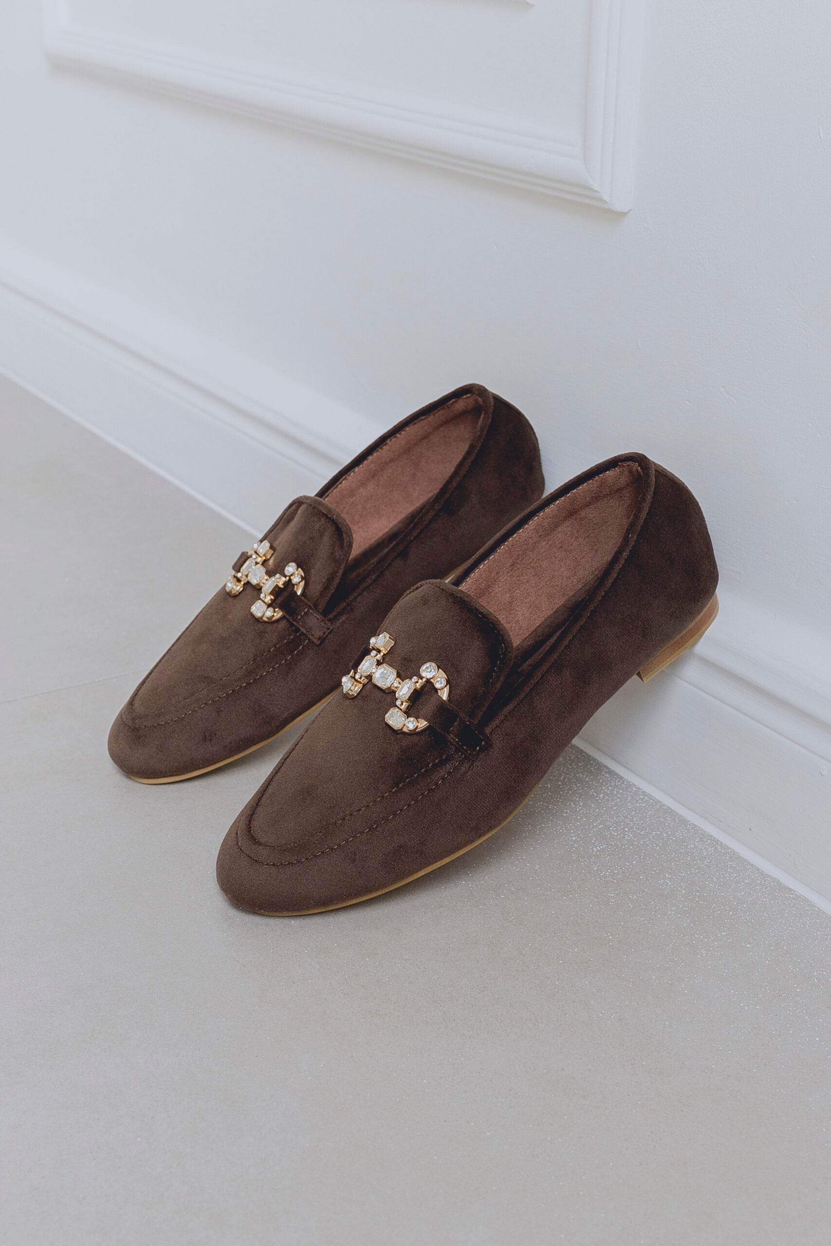 Pair of brown loafers with decorative elements on a light background