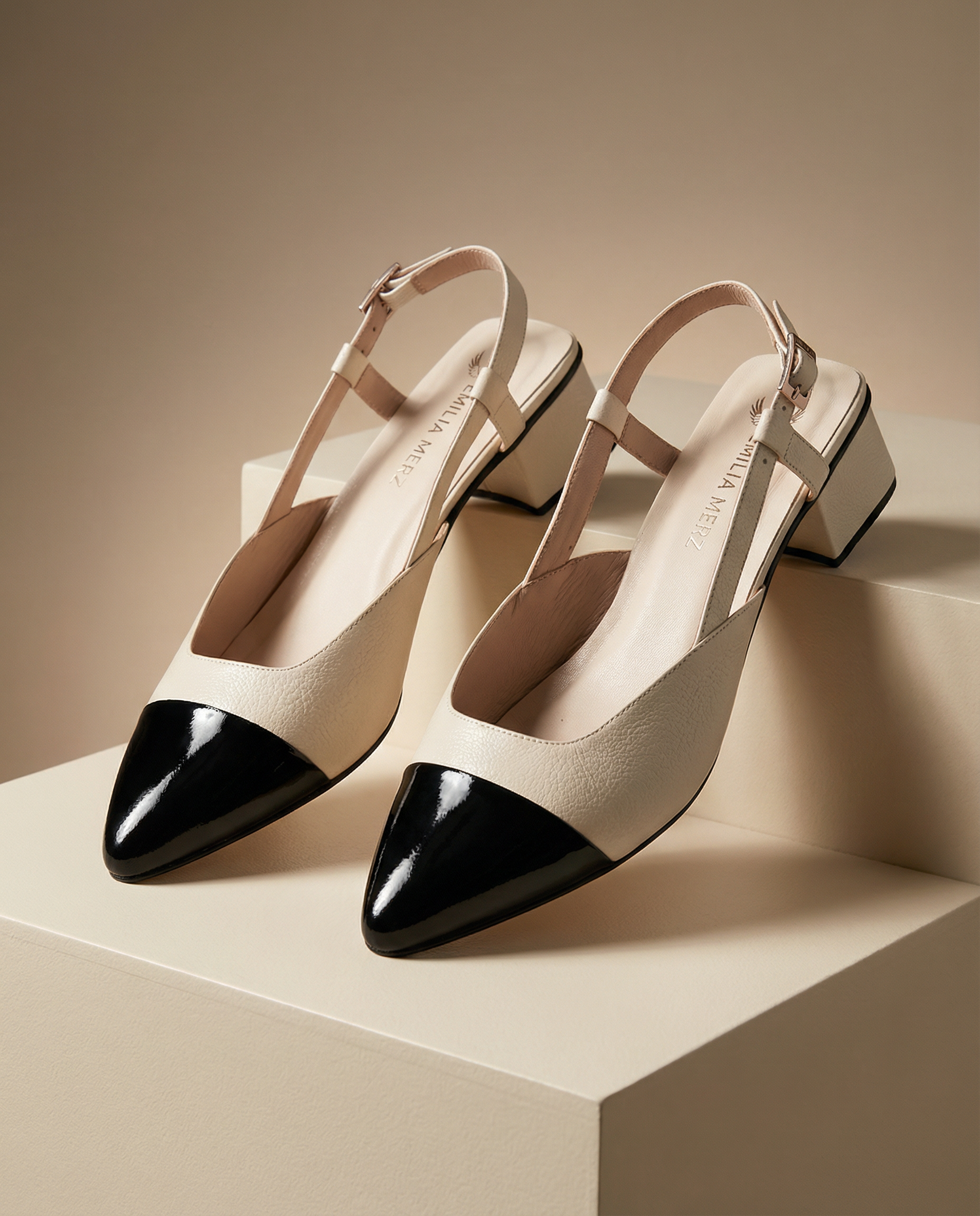 Pair of black and white pointed-toe shoes on a beige platform with a neutral background
