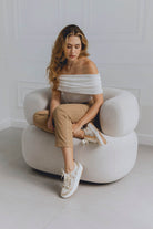 Woman sitting on a white chair in a minimalistic room wearing beige white sneakers for women with golden sprinkles