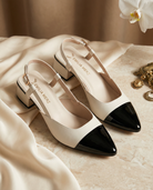White and black pointed-toe shoes on a beige fabric background.