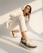 Woman wearing a white outfit with leopard print sneakers on a light background