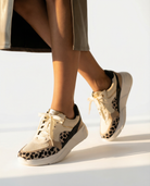 Person wearing beige sneakers with leopard print details on a white background