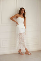 Woman wearing a strapless white top and lace skirt against a white wall with rosegold and silver two tone retro glam heels